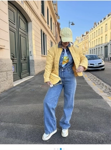 Outdoor street style view of a light yellow quilted jacket and denim jumpsuit outfit