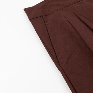 Détail d'un pantalon marron foncé montrant des plis et des poches sur tissu en lin