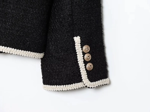 Close-up of black tweed jacket with white braided trim and gold lion relief buttons