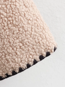 Detail of beige faux shearling fabric with black contrast braided edge and plush texture