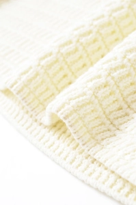 Close-up of off-white knit sweater showing ribbed cuffs and 3D square knit texture