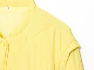 Detail of yellow quilted jacket with wave patterns and size label S on white background