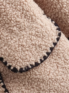 Detail of beige sherpa jacket showing plush teddy fleece texture and black blanket stitch edges