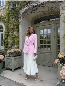 Détail d'un blazer rose avec taille nouée à fleur 3D et une jupe plissée blanche