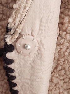 Detail of quilted beige sherpa jacket featuring metal rivet and thick contrast stitching