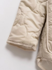 Detailed view of beige quilted sleeve with textured braided trim and wave stitching