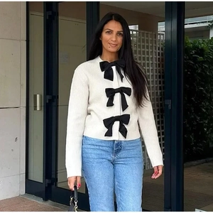 Dettaglio del cardigan bianco in maglia con tre grandi fiocchi in raso nero applicati