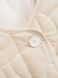 Macro shot of quilted cream cotton jacket fabric with resin button and woven texture binding