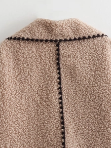 Close-up of beige faux shearling jacket featuring decorative black contrast stitching