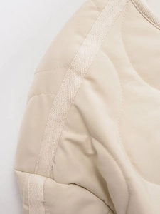 Macro detail of beige quilted air cotton jacket featuring curved stitching and woven trim
