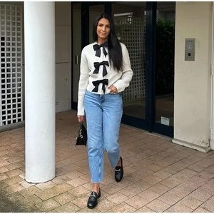 Elegante cardigan in maglia crema con tre grandi fiocchi neri abbinato a jeans casual