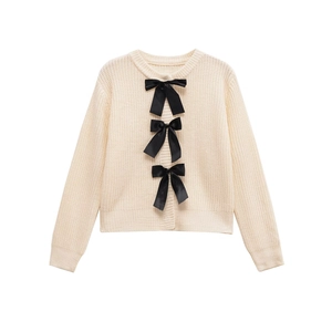 Elegante cardigan in maglia crema con tre grandi fiocchi di raso nero su sfondo bianco puro
