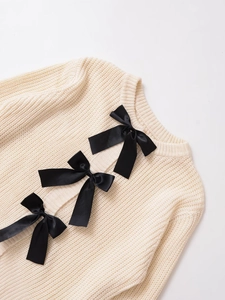 Dettaglio del cardigan in maglia panna con grandi fiocchi di raso nero e girocollo