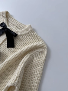 Dettaglio del cardigan in maglia crema con fiocco in raso nero e scollo rotondo a coste