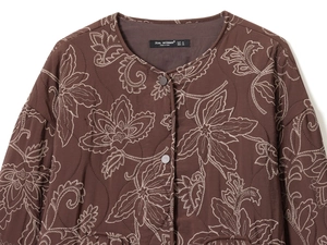 Détail de broderie florale blanche sur une veste matelassée marron à col rond boutonné