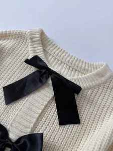 Dettaglio del cardigan in maglia crema con elegante fiocco in raso nero sulla scollatura