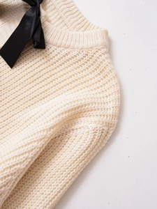 Dettaglio del cardigan in maglia bianco sporco con fiocchi decorativi in raso nero
