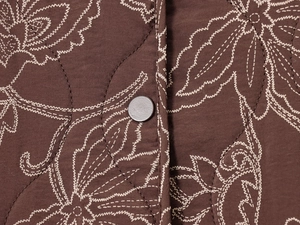Détail du tissu matelassé marron foncé avec broderie florale blanche et bouton-pression mat