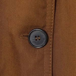 Close-up of brown pleated coat with textured twill fabric and black round button detail