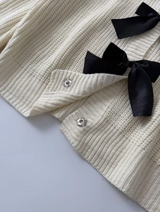 Dettaglio del cardigan in maglia crema con fiocchi in raso nero e bottoni a pressione