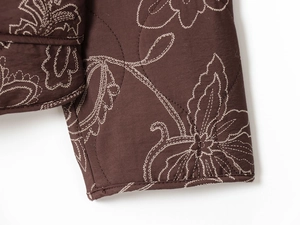 Détail d'une veste matelassée marron chocolat avec broderies florales blanches et surpiqûres