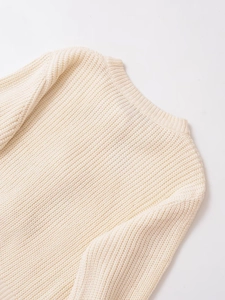 Dettaglio del cardigan in maglia crema con trama a coste e cuciture sulle spalle rifinite