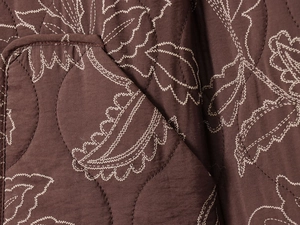 Gros plan sur le tissu matelassé marron avec broderie de feuilles et coutures fines