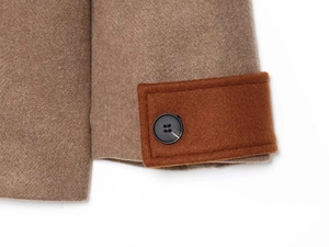 Macro detail of camel wool coat sleeve with dark brown decorative strap and black button