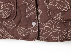 Détail de la veste matelassée marron foncé avec broderie florale et bouton métallique