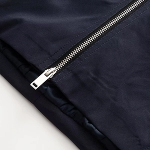 Detail view of a silver metal rectangular zipper on dark blue twill fabric jacket