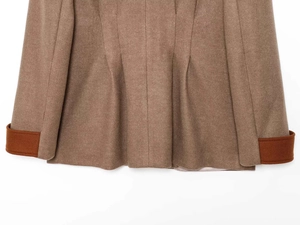 Detail of wool coat fabric with camel and brick red contrast stitching and pleated hem