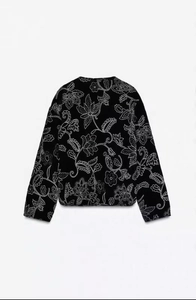 Detail of white floral embroidery on black round neck jacket with intricate stitch patterns