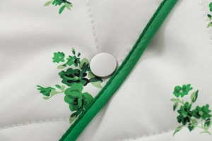 Macro detail of quilted cotton fabric with green floral print and silver snap button