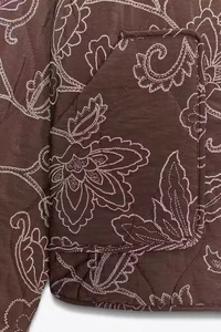 Close-up of brown quilted jacket featuring white paisley embroidery and side patch pocket