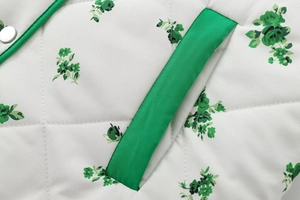Detail of floral printed quilted jacket featuring green trim pocket and metal snap button