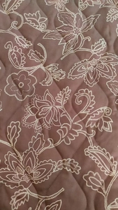 Detailed macro view of diamond quilted fabric with white floral embroidery on dark brown