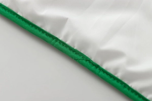 Macro detail of high-density white fabric with emerald green binding and reinforced stitching