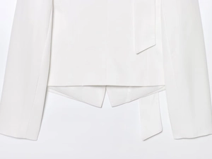 Detailed view of white blazer with asymmetrical hem and decorative waist belt detail