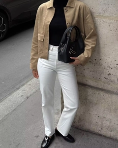 Détail d'une veste en daim camel portée avec un jean blanc et un sac en cuir noir