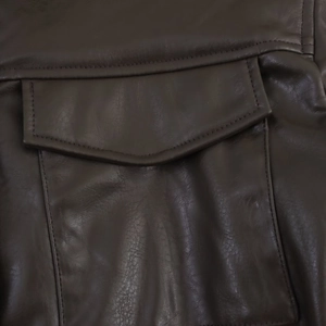 Close-up of deep brown faux leather jacket featuring detailed V-shaped flap pocket and stitching
