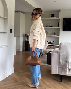 Chic beige faux shearling jacket paired with blue jeans and a brown leather handbag