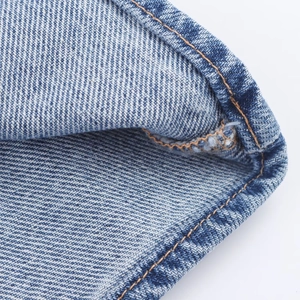 Close-up detail of mid-blue denim fabric with contrast orange stitching and twill texture
