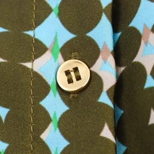 Macro detail of geometric print satin fabric with a polished gold metallic button fastener