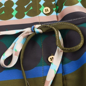 Detailed close-up of satin shirt with abstract print, gold buttons, and waist tie bow