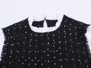 Detail eines Tweed-Tops mit weißem Rüschenkragen und Fransenrändern in klassischem Schwarz-Weiß
