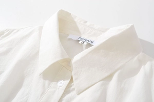Détail du col d'une chemise blanche brodée avec étiquette de marque et bouton résine