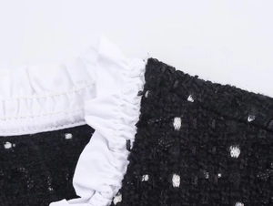 Detailansicht von schwarzem Tweed-Stoff mit weißem Volant-Besatz und Nahtdetails
