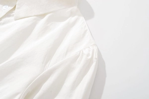 Gros plan du col de chemise en coton blanc avec bouton et détails plissés sur l'épaule