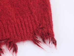 Macro detail of red cable knit sweater featuring distressed hem and ribbed textures