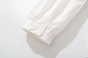 Détail du poignet d'une chemise blanche avec des plis délicats et un bouton assorti